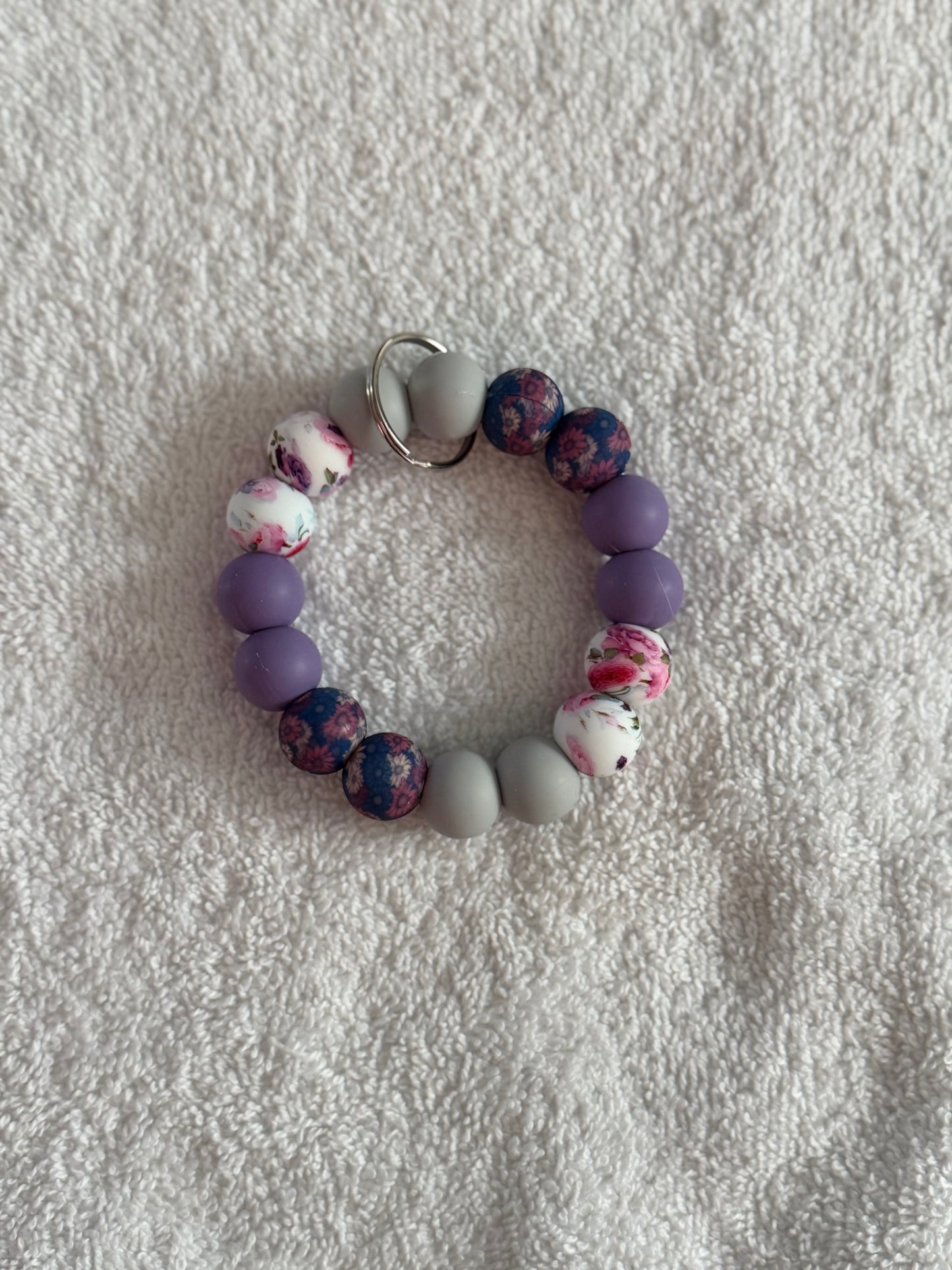 Beaded bracelet with purple, gray, and floral beads on a textured white surface