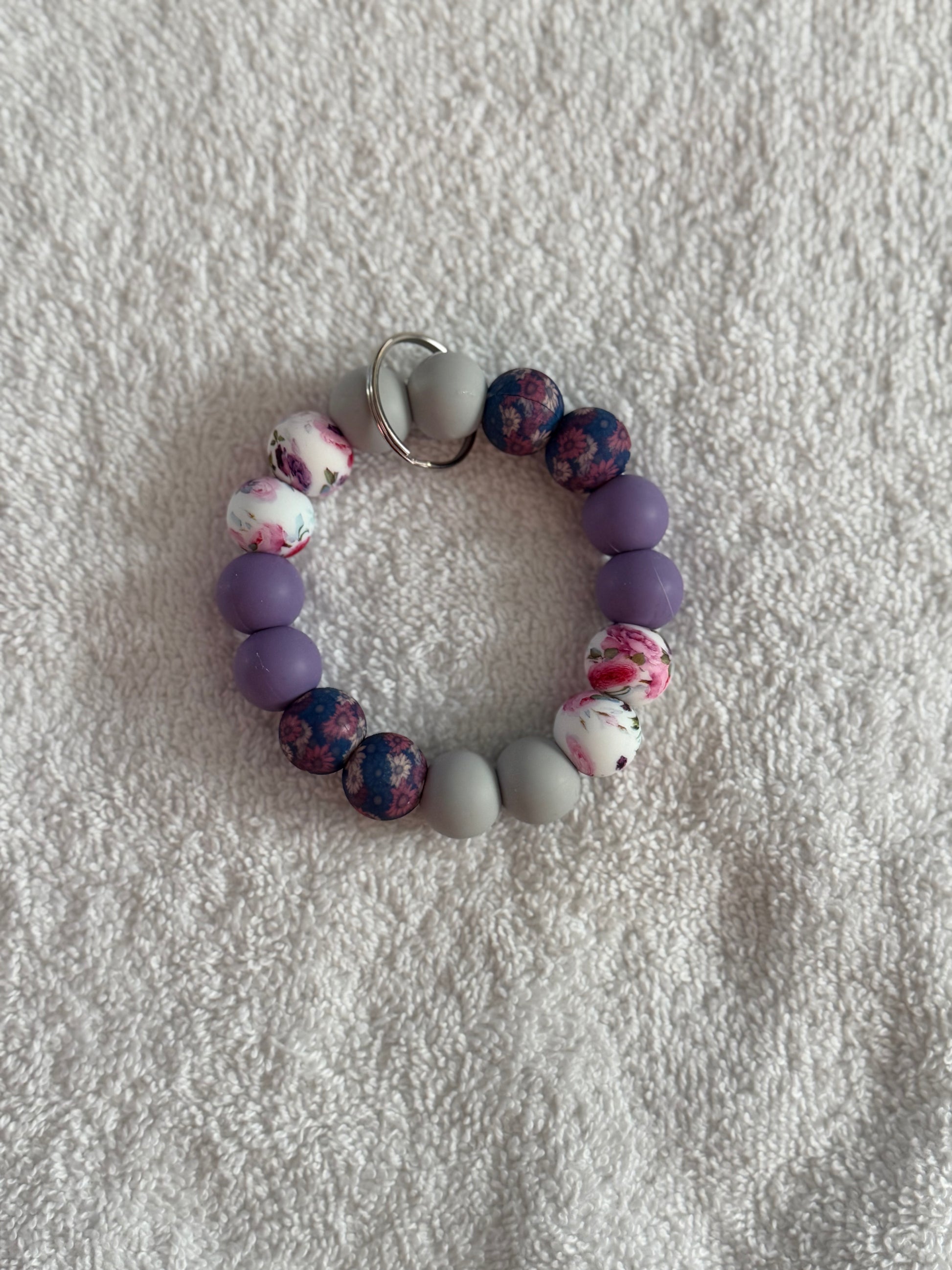 Beaded bracelet with purple, gray, and floral beads on a textured white surface