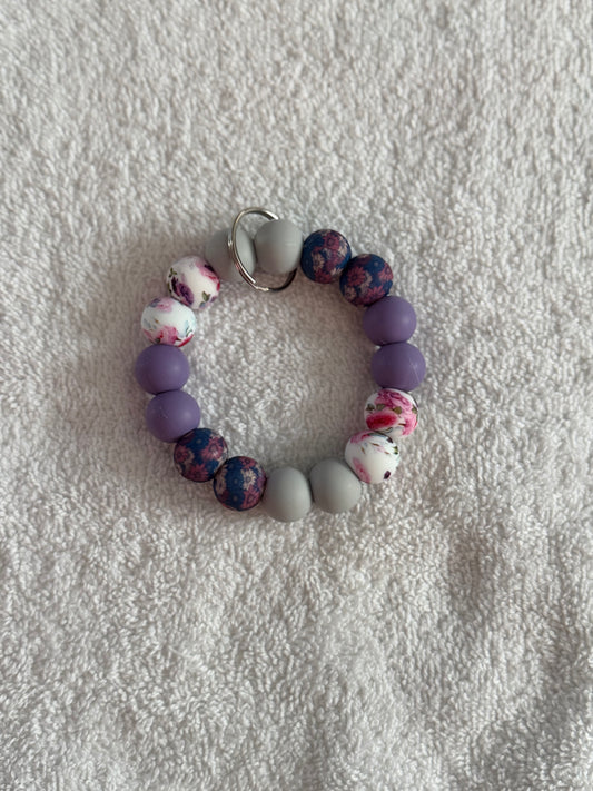 Beaded bracelet with purple, gray, and floral beads on a textured white surface